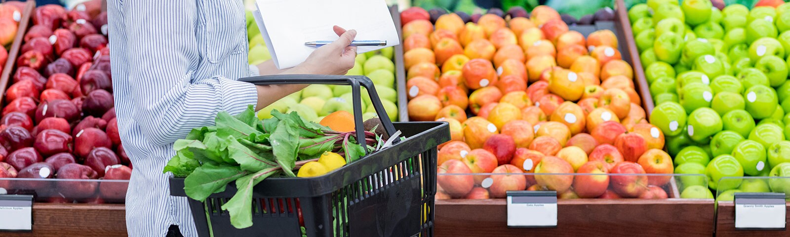 Woman grocery shopping next to a row of apples