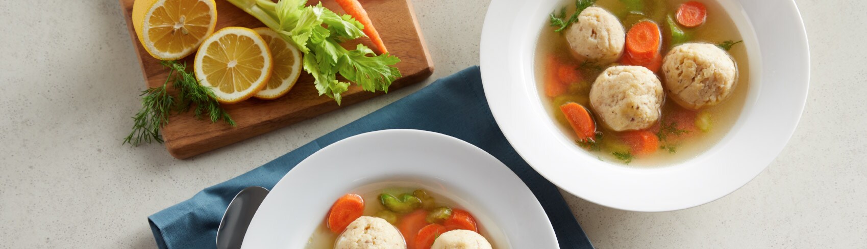 Matzo ball soup in a white bowl with fresh ingredients on the side
