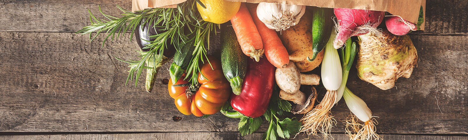 Fresh produce is a browl paper bag on a wooden table