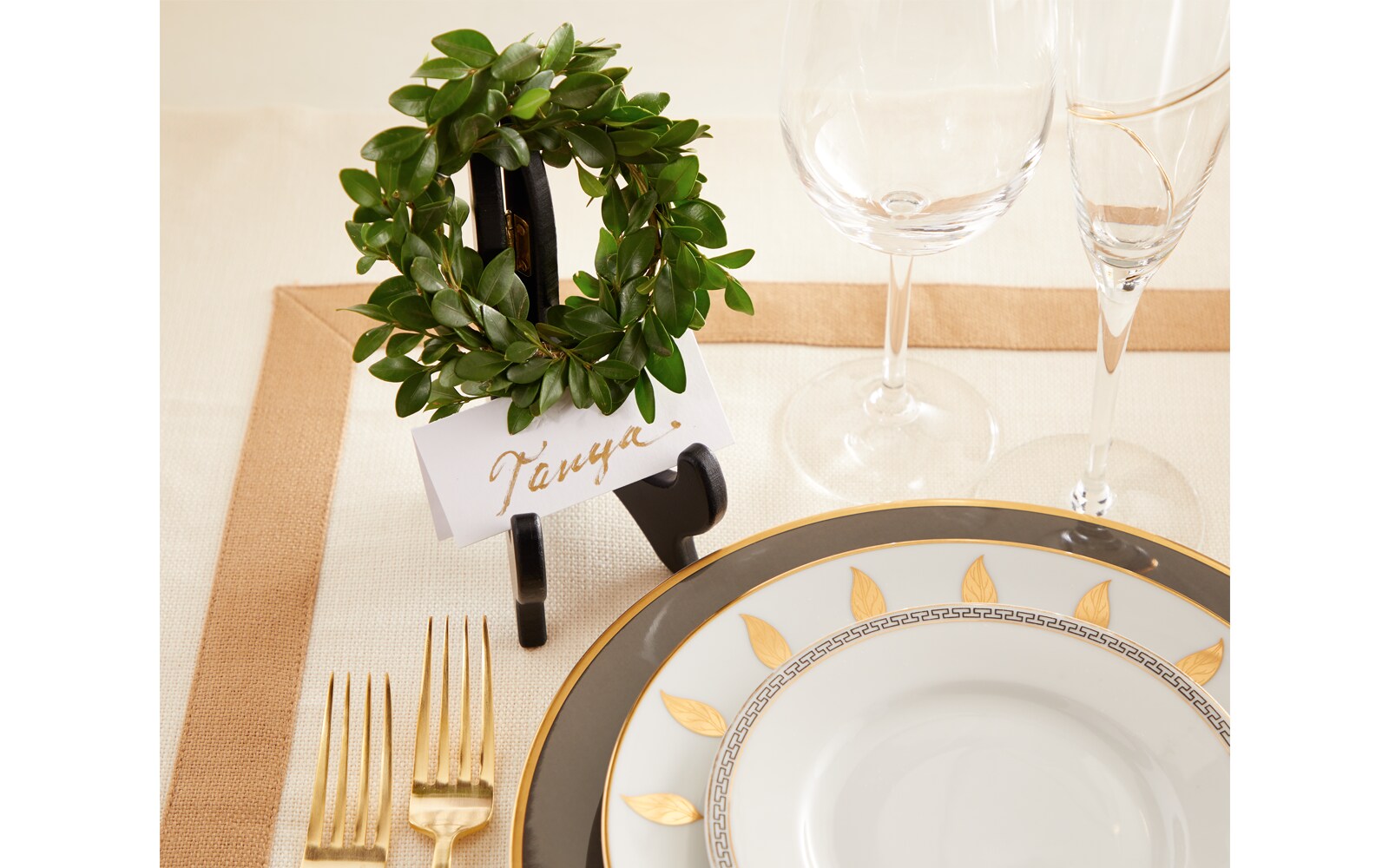 A name card sits in a small picture frame holder with a tiny wreath at the top, beside this is an ornate dinner plate setting