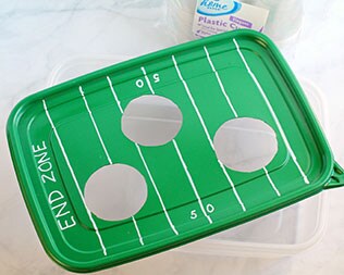 Decorated green rectangle container lid with 50-yard line and end zones drawn in white marker