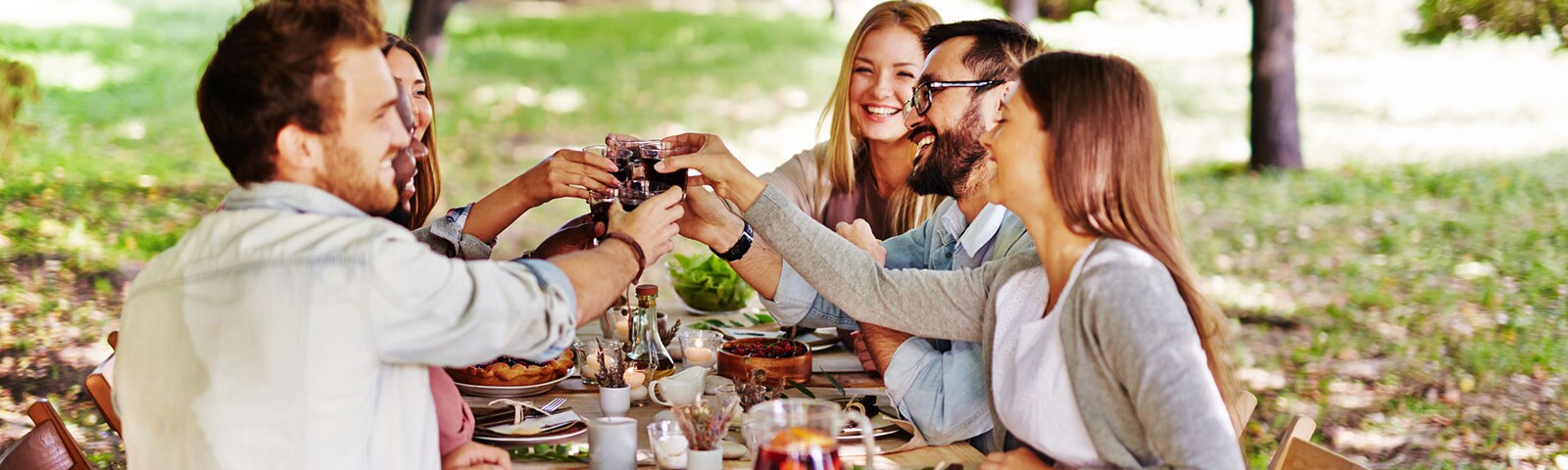 Group of friends sitting around an outdoor table sharing a friendsgiving feast and toasting one another